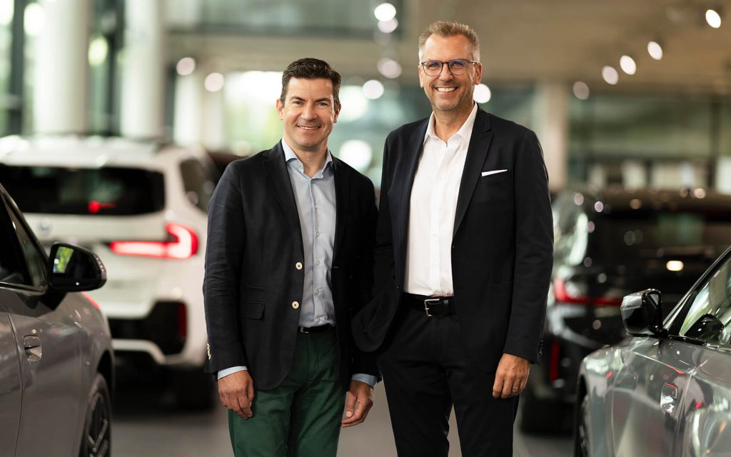 Zwei Mitarbeiter stehen nebeneinander zwischen geparkten Autos