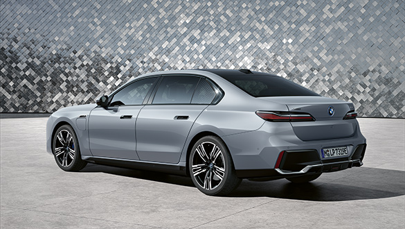 BMW 7er Limousine Plug-in-Hybrid in Silber aus schräger Heckansicht vor silberner Mosaikwand.