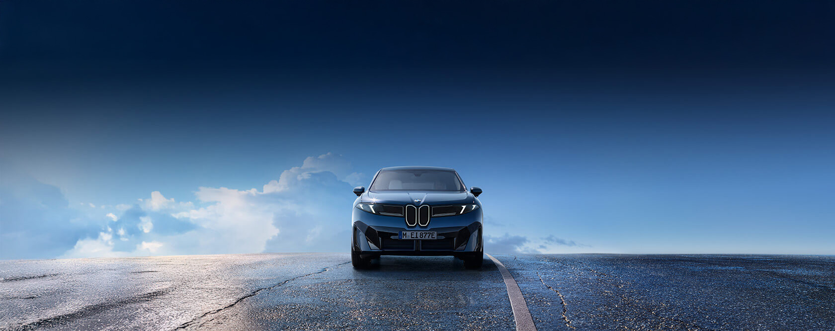 Blauer BMW iX3 steht frontal auf einer Straße. Im Hintergrund ist eine freundlicher blauer Himmel mit Wolken zu sehen.