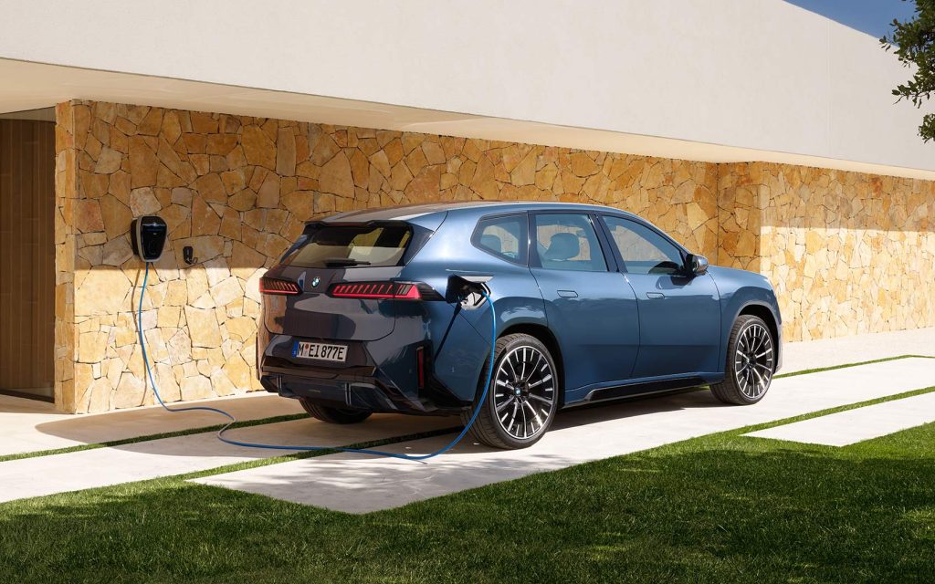 Blauer BMW iX3 wird an einer Hauswand per Wallbox geladen