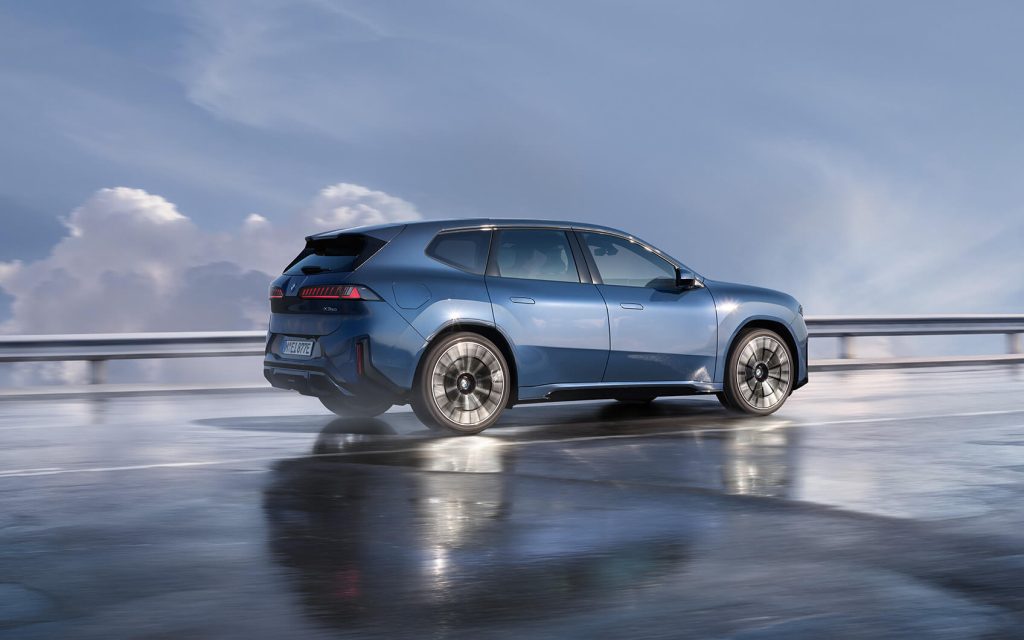 Blauer BMW iX3 in Seitenansicht auf einer Straße. Im Hintergrund ist eine freundlicher blauer Himmel mit Wolken zu sehen.
