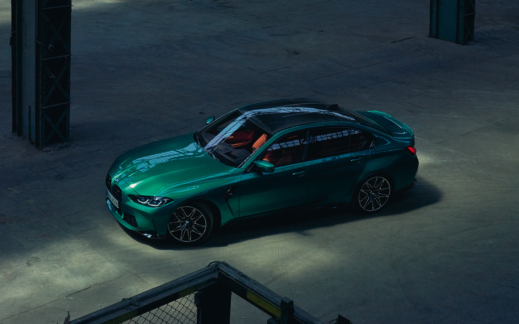 Grüne BMW M3 Limousine in leerer Industriehalle bei gedämpftem Licht.