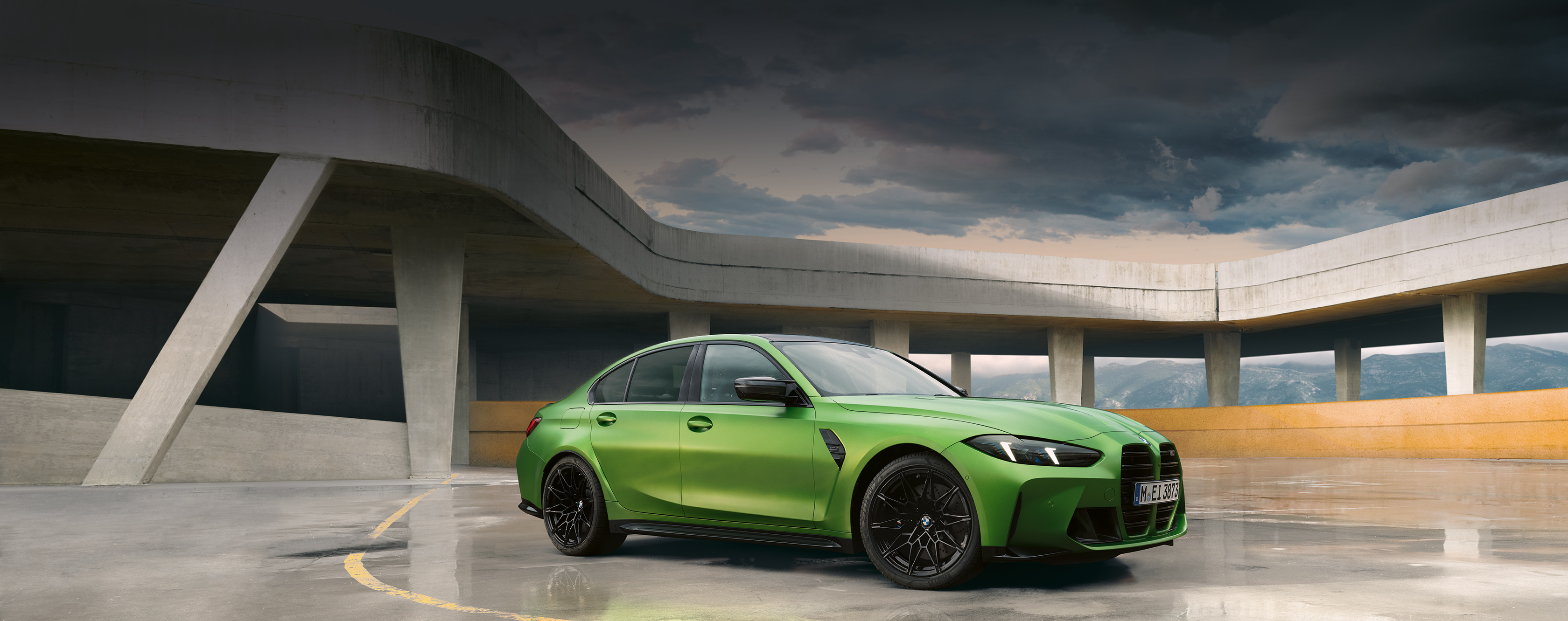 Grünes BMW 3er Limousine M Automobil in futuristischem Parkhaus, bewölkter Himmel und Berge im Hintergrund