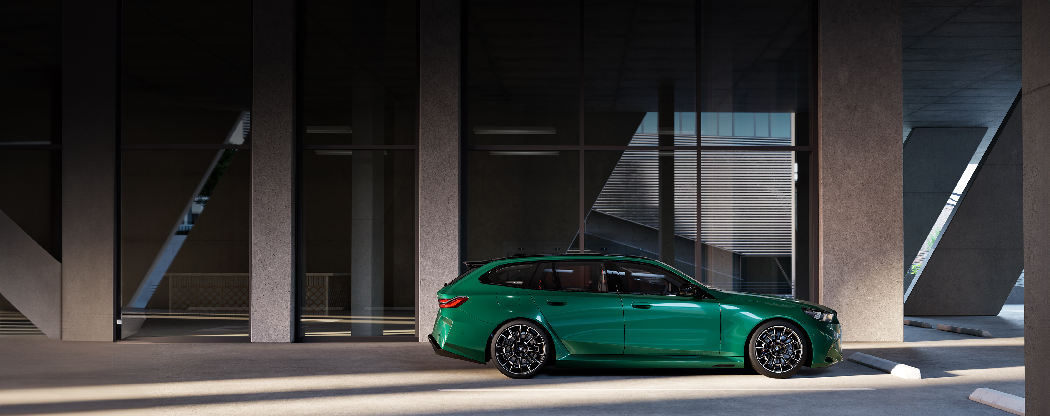 Profilaufnahme des BMW M5 Touring in der Farbe Grün, parkend vor einem modernen Gebäude