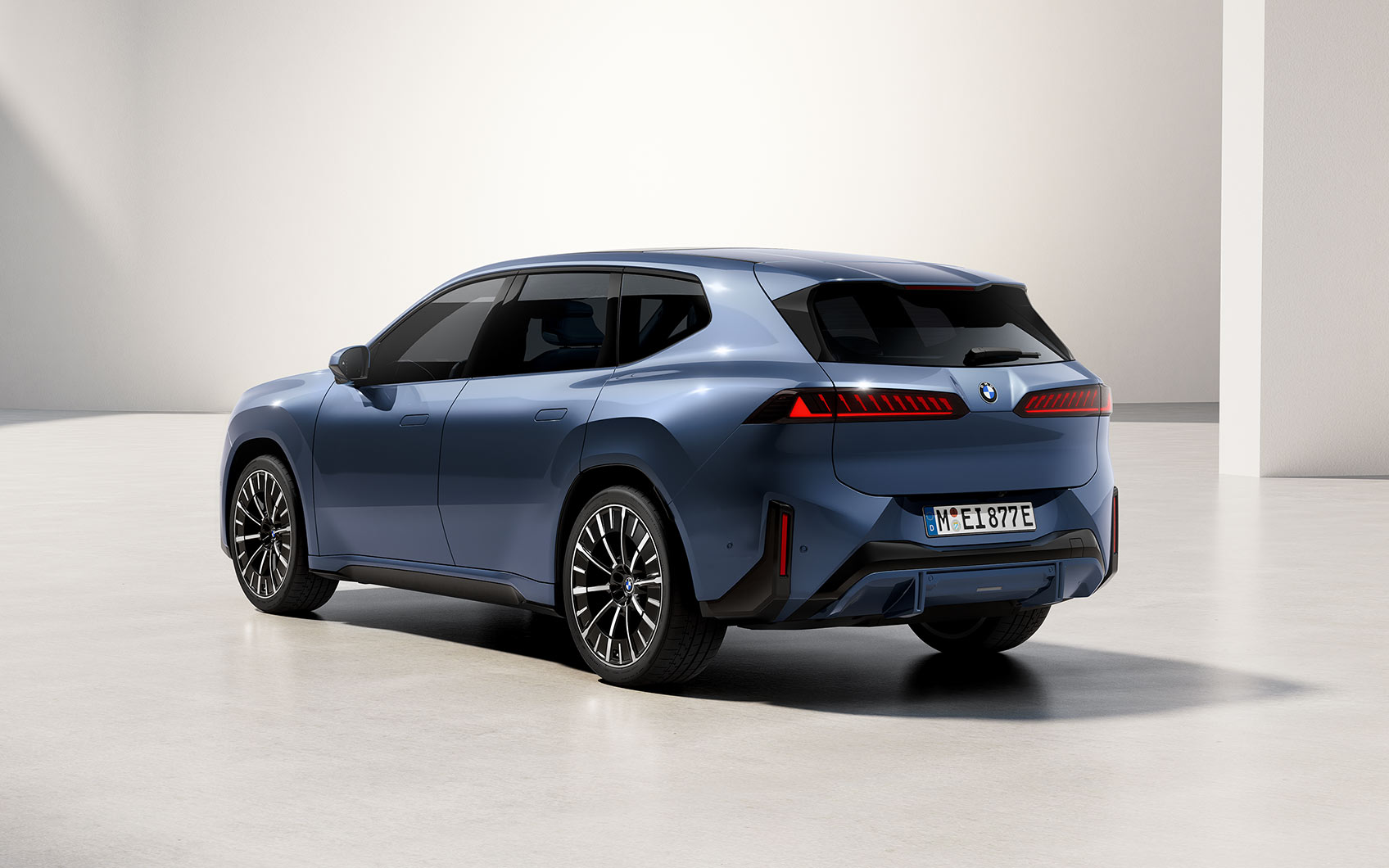 Blauer BMW iX3 von schräg hinten mit sichtbarer Fahrerseite in heller Studio-Umgebung.