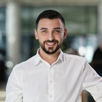 Junger Mann mit Bart im Autohaus, trägt weißes Hemd und lächelt in die Kamera