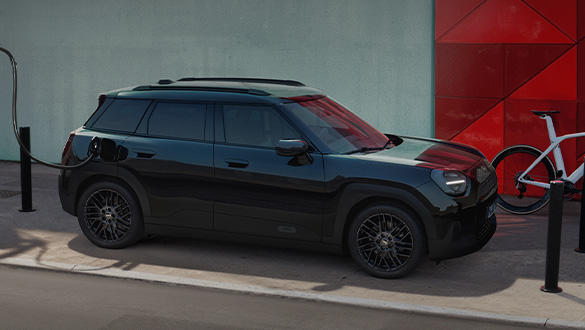 MINI Aceman Blackyard parkend am Straßenrand in urbaner Umgebung mit angeschlossenem Ladekabel