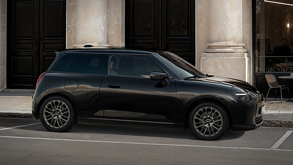 Seitenansicht eines schwarzen, elektrischen MINI Coopers vor einem Gebäude mit Säulen und dunklen Türen.