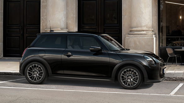 Seitenansicht eines schwarzen MINI Coopers vor einem Gebäude mit Säulen und dunklen Türen.