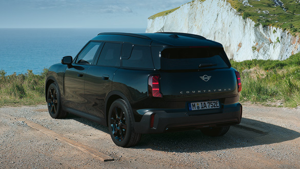 Heckansicht eines schwarzen MINI Countryman Electric auf einem Küstenweg mit Klippen und Meer im Hintergrund.