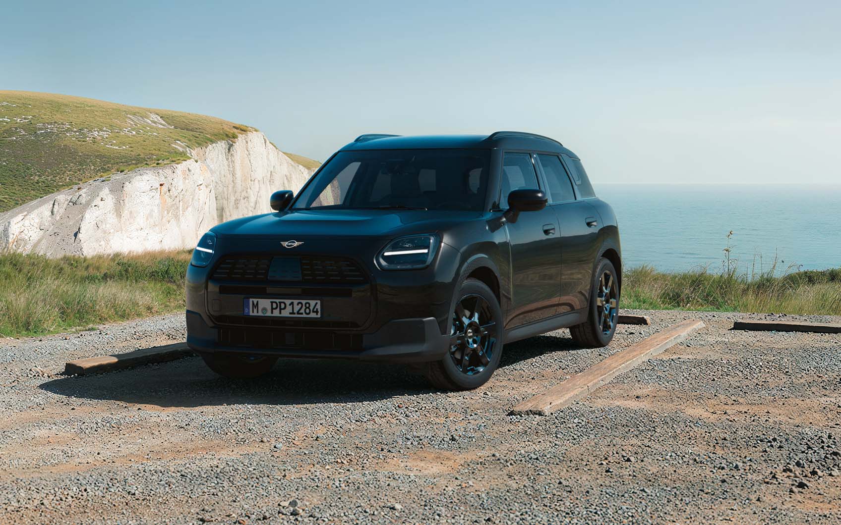 MINI Countryman Blackyard parkend auf einem Schotterplatz vor Küstenlandschaft mit Klippen und Meer.