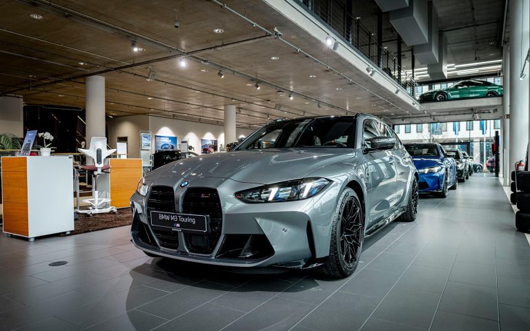 Grauer BMW M3 Touring im Autohaus, Frontansicht schräg von links