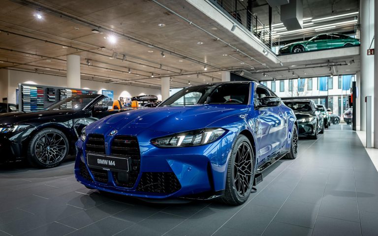 Blauer BMW M4 im Autohaus, Frontansicht schräg von links