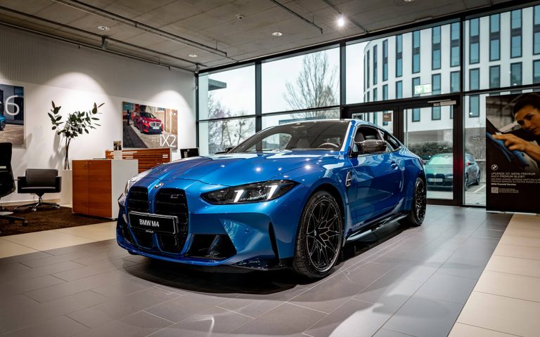 Blauer BMW M4 im Autohaus, Frontansicht schräg von links