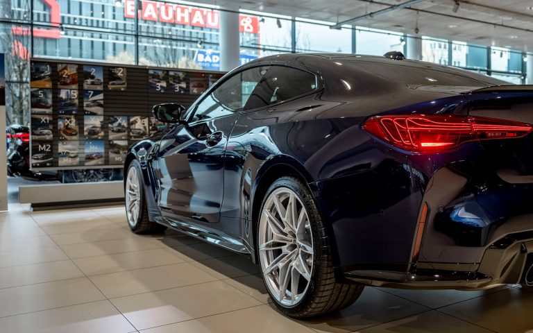 Blauer BMW M4 im Autohaus, Heckansicht schräg von links