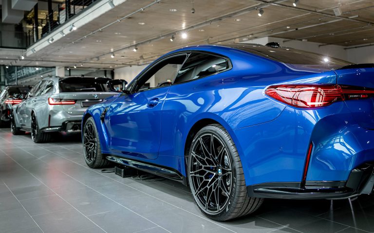 Blauer BMW M4 im Autohaus, Heckansicht schräg von links