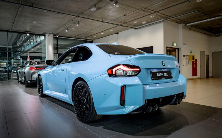 Hellblauer BMW M2 im Autohaus, Heckansicht schräg von links