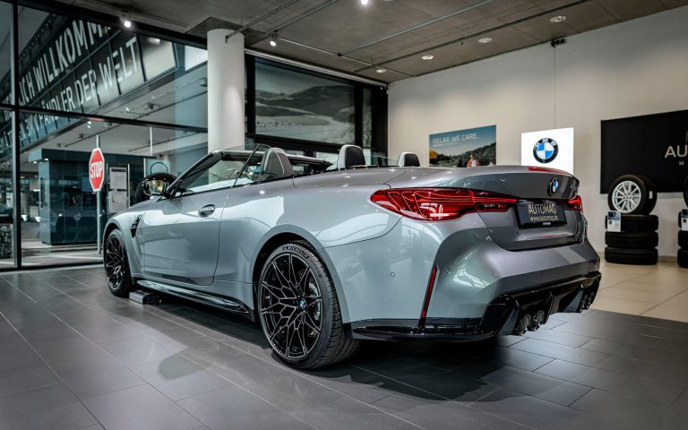 Graues BMW M4 Competition Cabrio im Autohaus, Heckansicht schräg von links