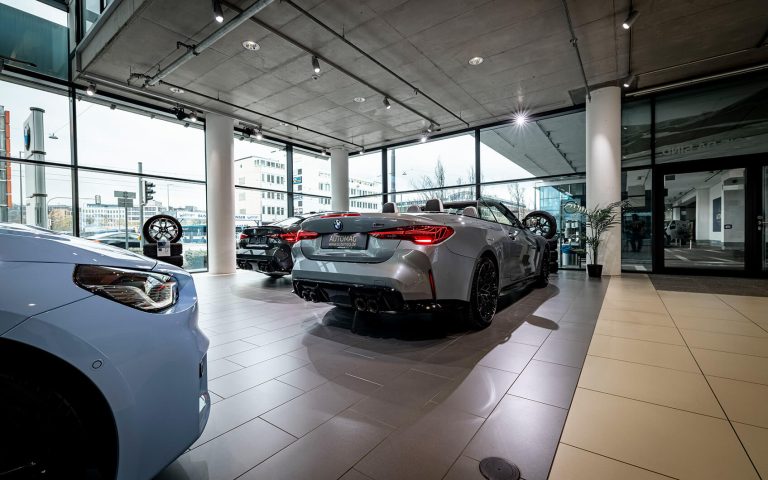 Graues BMW M4 Competition Cabrio im Autohaus, Heckansicht mit weiteren BMW Modellen