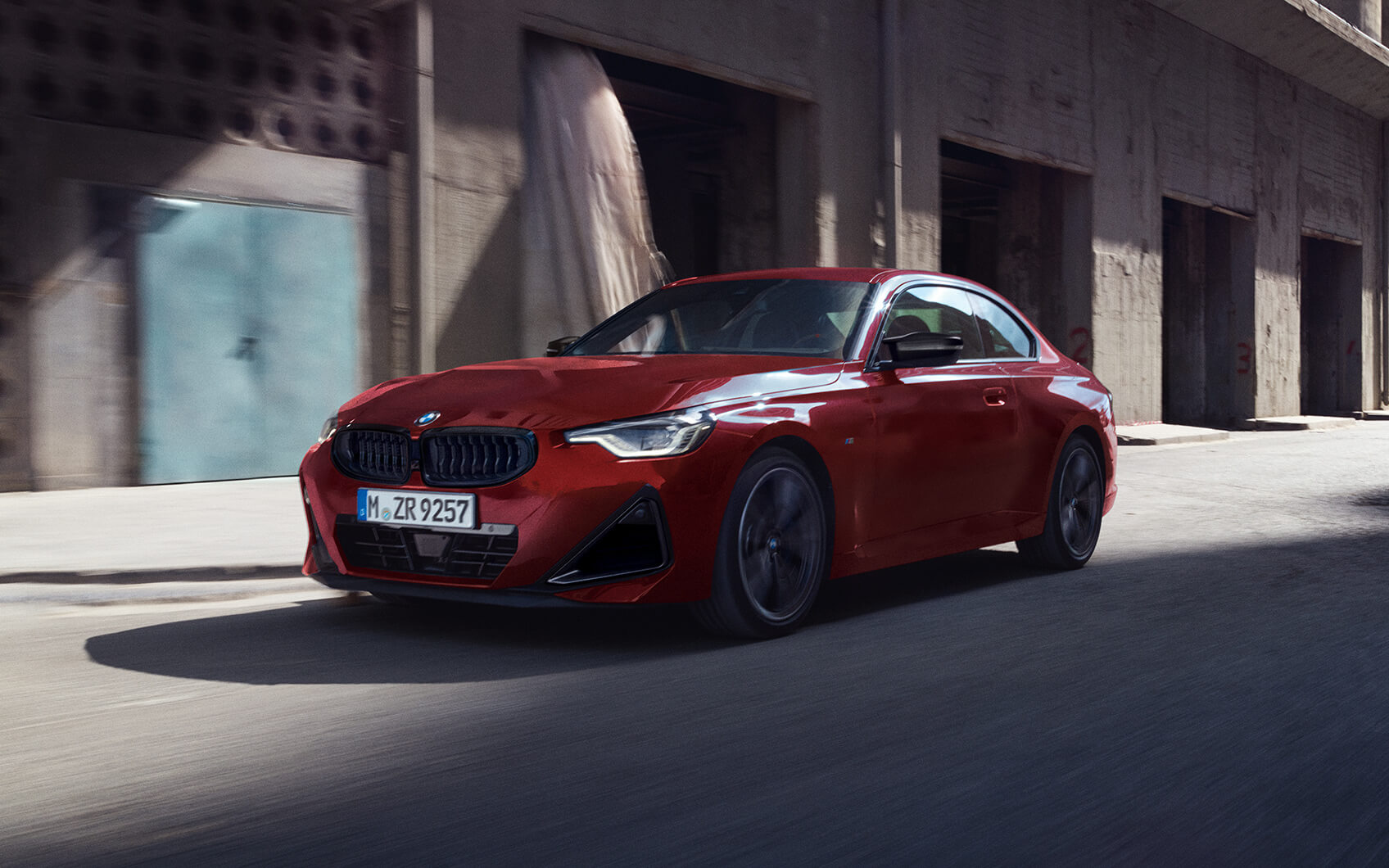 Rotes BMW 2er Coupé fährt durch ein urbanes Industriegebiet