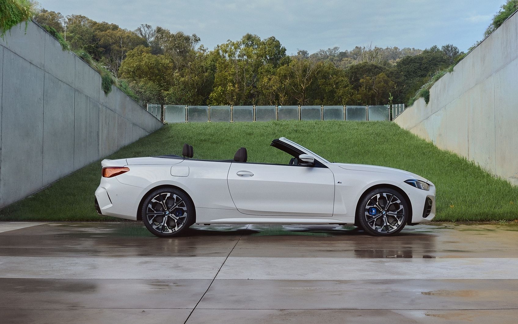 Weißes BMW 4er Cabrio mit offenen Verdeck parkt nach Regen neben Betonmauer und Grasböschung