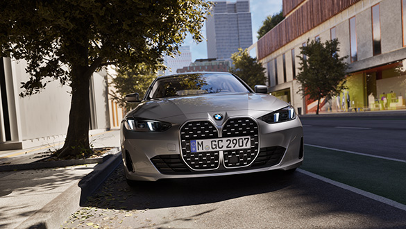 Frontansicht eines grauen BMW 4er Gran Coupé parkend auf einer Straße im urbanen Raum mit Bäumen, Fokus auf Grill und Scheinwerfer