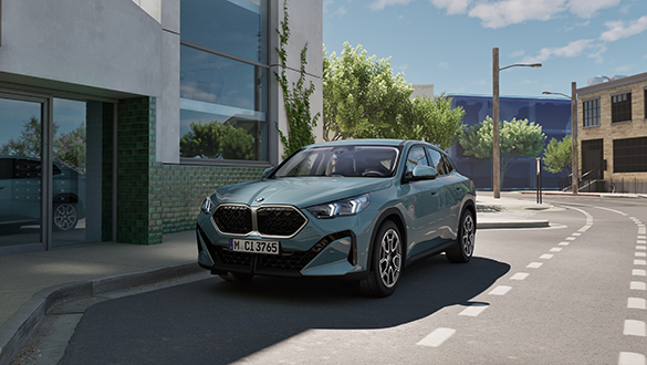 Grüner BMW X2 parkt an urbanem Straßenrand vor hohem Gebäude, Front und Fahrerseite sichtbar