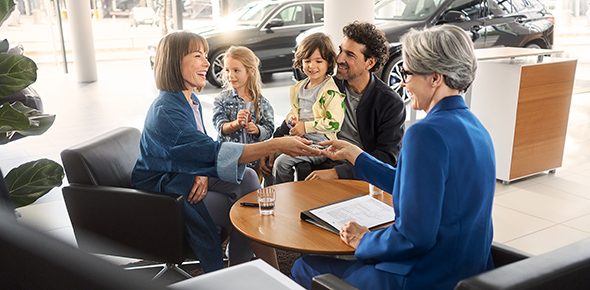 Mutter, Vater und zwei Kleinkinder sitzen mit BMW Verkäuferin in Autohaus