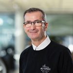 Mann mit Brille im Autohaus, trägt schwarzen Pullover mit Logo „AUTOMAG München“