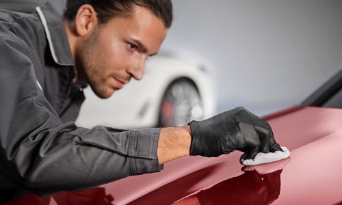 Mann poliert roten Autolack mit Tuch und schwarzen Handschuhen.