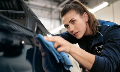 BMW-Mitarbeiterin reinigt konzentriert den Lack eines Fahrzeugs mit einem Mikrofasertuch