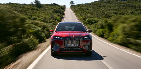 Frontansicht des roten BMW iX, fahrend auf Landstraße in idyllischer Landschaft