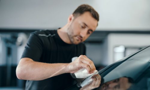 BMW-Werkstattmitarbeiter reinigt Autoscheibe mit weißem Tuch in Werkstattumgebung.