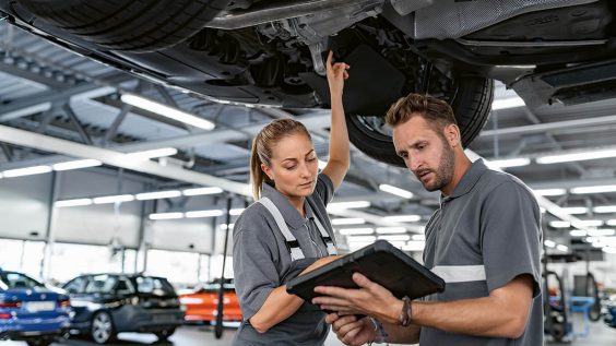 Zwei BMW Servicemitarbeiter inspizieren Fahrzeugunterboden in Werkstatt.