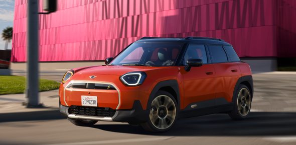 MINI Aceman in der Farbe Orange auf der Straße vor einem pinken Gebäude