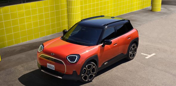 Vogelperspektive auf einen orangenen MINI Aceman, geparkt vor einer gelben Wand in einem Parkhaus