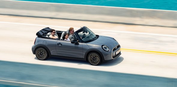 mini-cabrio-teaser Blick von oben auf ein fahrendes MINI Cooper Cabrio in der Farbe Grau auf einer Küstenstraße mit Meer im Hintergrund