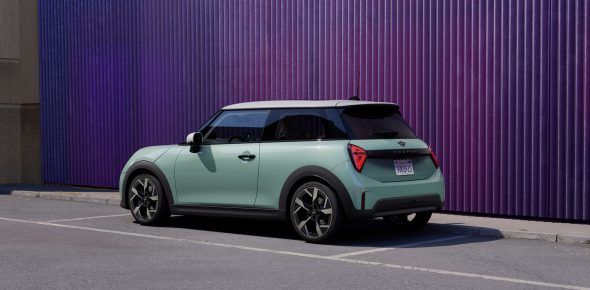 Mintgrüner Mini Cooper mit weißem Dach auf einem Parkplatz vor lila Wand
