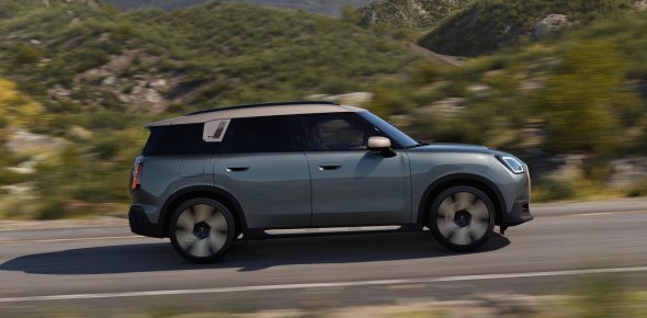 mini-countryman-teaser Grüner Mini Countryman mit weißem Dach fährt auf Landstraße vor Bergkulisse.